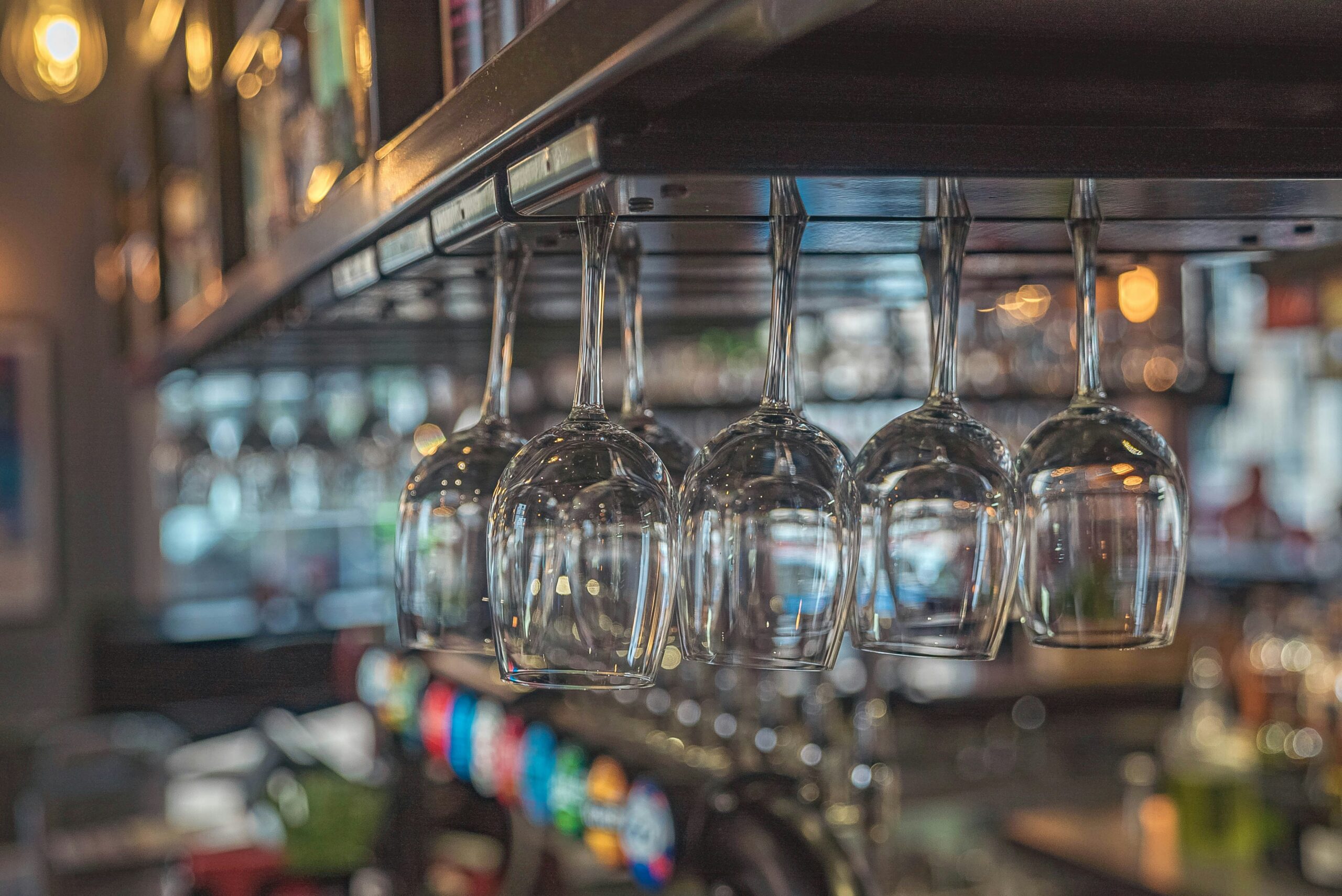 Picture shows some wine glasses hanging upside-down with a faded image of a bar in the background
