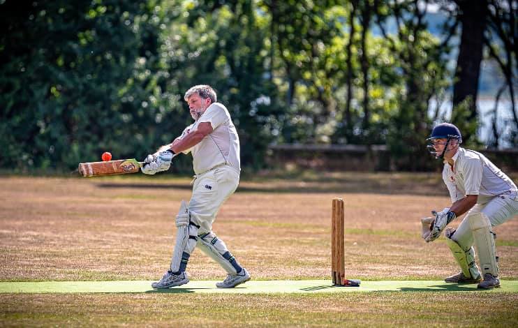 Picture shows two men playing cricket. One is hitting the ball and behind him stands the wicket keeper