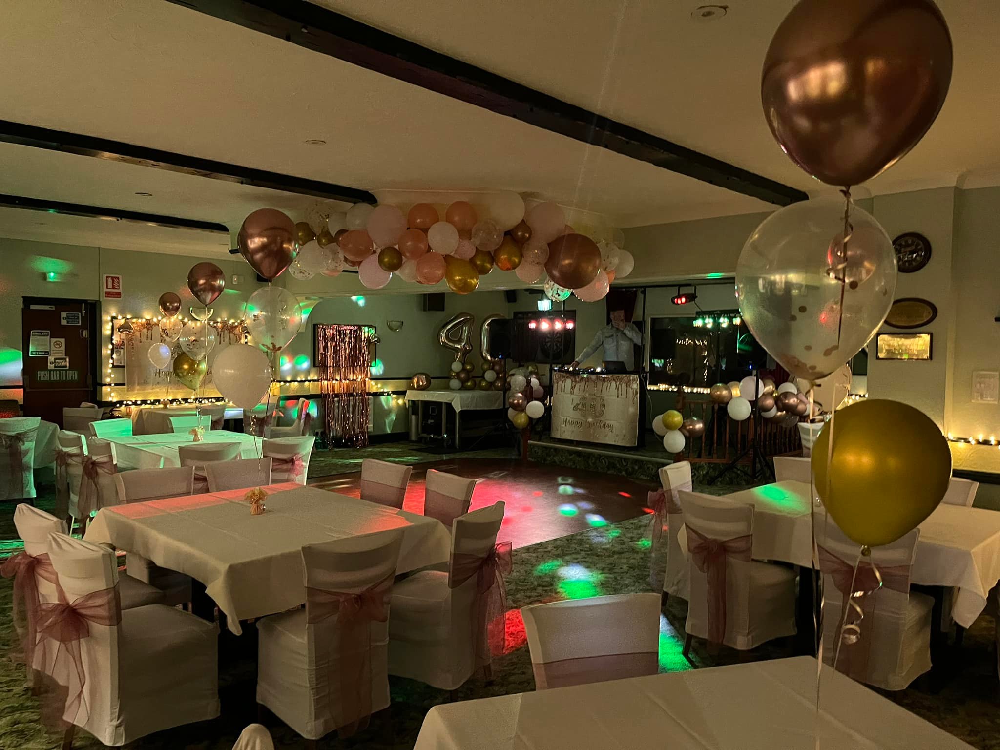 Picture shows some nicely laid tables ready for a party. There are balloons decorating the room and disco lighting is reflecting on the tables